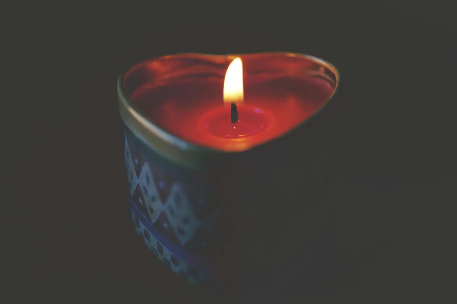 Heart-shaped candle with warm, glowing flame creating a romantic atmosphere.